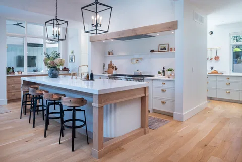 Painted kitchen with a long white island, timber beam over the range and black lantern pendants
